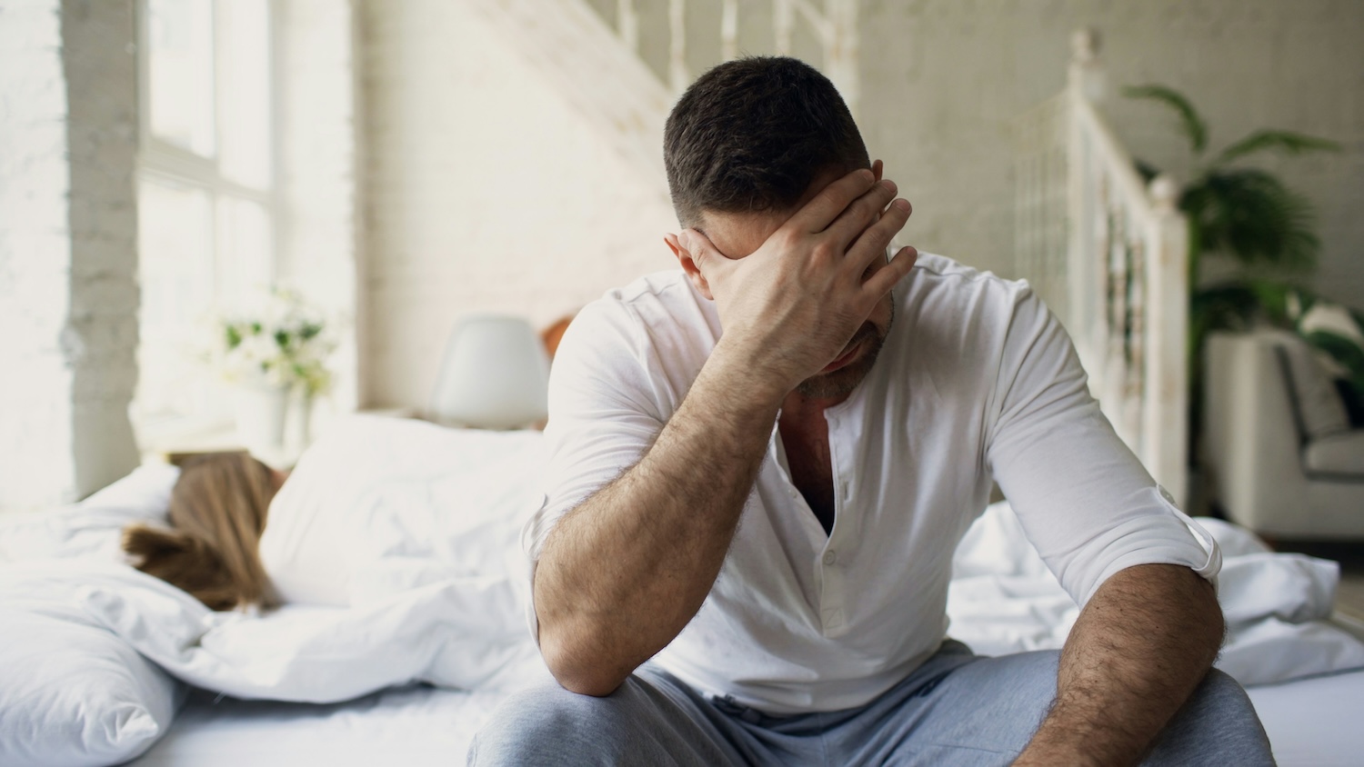 Couple in a bedroom with one partner visibly distressed and the other turned away, representing conflict and emotional disconnection in a relationship.