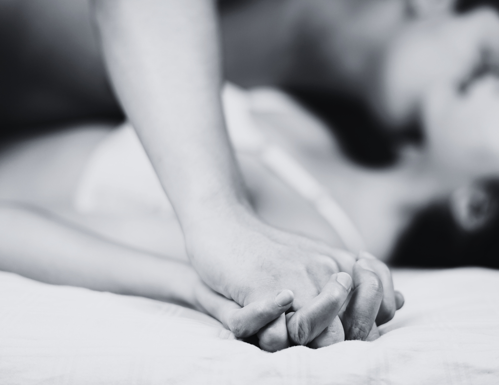 Couple holding hands in bed, representing vulnerability, trust, and emotional safety during intimacy.